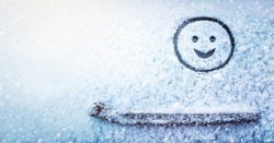 Banner of smiling face (symbol) painted on snow above windshield wiper of car. Winter, transport concept. Copy space. Empty place for your message.