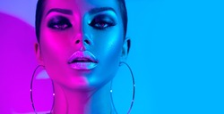 High Fashion model metallic silver lips and face woman in colorful bright neon uv blue and purple lights, posing in studio, beautiful girl, glowing make-up, colorful make up. Glitter Vivid neon makeup