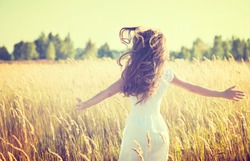 Beauty Girl Outdoors enjoying nature. Beautiful Teenage Model girl in white dress running on the Spring Field, Sun Light. 