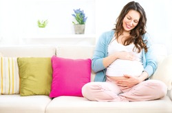 Pregnant Happy smiling Woman sitting on a sofa and caressing her belly. Mom Expecting Baby. Pregnant Woman Belly. Pregnancy. Beautiful Pregnant Woman. Maternity concept. Baby Shower 