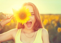 Beauty joyful teenage girl with sunflower enjoying nature and laughing on summer sunflower field. Sunflare, sunbeams, glow sun. Backlit.