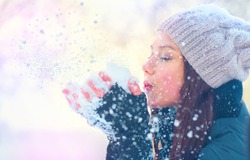 Winter girl blowing snow. Beauty Joyful Teenage Model Girl having fun in winter park. Beautiful young woman laughing outdoors. Enjoying nature.