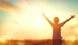 Little boy raising hands over sunset sky, enjoying life and nature. Happy Kid on summer field looking on sun. Silhouette of male child in sunlight rays. Fresh air, environment concept. Dream of flying