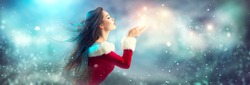Christmas Winter Fashion Girl blowing  Magic snow in Her Hand. Fairy. Beautiful New Year and Xmas Tree. Holiday Hairstyle, Makeup. Gift. Beauty Model woman on Holiday Blurred blue Background, sale