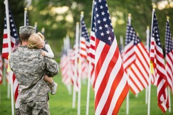 Handsome American Soldier in uniform hugging his 2 year old daughter standing in a field of flags