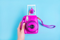 Woman hand holding purple instant camera isolated on blue background.