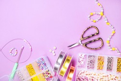 Creative flatlay of different pearl beads with tools for making jewelry, wire string and scissors isolated on pink background.