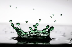 A drop of green water forming a coronet as it splashes into a shallow layer of liquid