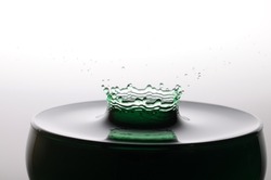 A drop of green water forming a coronet as it splashes into a glass full of liquid
