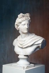 God Apollo bust sculpture. Ancient Greek god of Sun and Poetry Plaster copy of a marble statue on grange concrete wall background