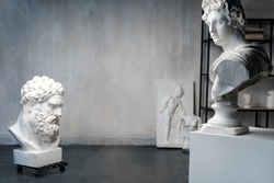 God Apollo bust sculpture and bust of the Farnese Hercules. Head sculpture, plaster copy of a marble statues of Greek gods and heroes on grange concrete wall background in studio. Copyspace for text.