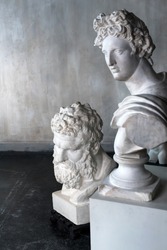 God Apollo bust sculpture and bust of the Farnese Hercules. Head sculpture, plaster copy of a marble statues of Greek gods and heroes on grange concrete wall background in studio. Copyspace for text