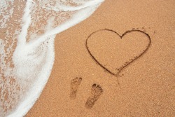 Shape of the heart and footprints in the sand on the beach