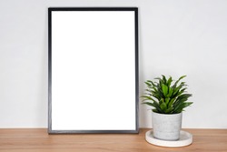 Black wooden vertical frame with white blank card and green plant in concrete pot on wooden table on gray wall background. Mockup, template for your design, free copy space for text