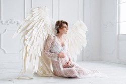 Beautiful young pregnant girl with big angel wings in white studio.