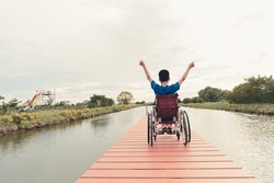 Behind of young man with disability relaxing on wooden bridge jutting into the lake at the outdoor vacation in summer, People leisure travel and mental healthy concept.