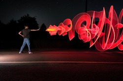 A man in the road at the middle of the night shooting out a graffiti-like artistic laser blast powers from his hand