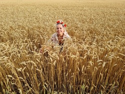 young woman posing in agriculture rye or barley or wheat field. girl wearing flower wreath on head. nature lover. summer wallpaper.