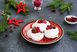 Portion Pavlova meringue pastries with cream and cranberry sauce in New Year's or Christmas decor on a red plate on a dark concrete background. New Year and Christmas desserts. Selective focus