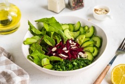 Vegetable salad with beetroot leaves, cucumber, green onions and pickled beets, dressed with olive oil, in a ceramic bowl on a light concrete background. Vegan Recipes. Healthy food