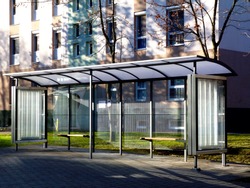 bus shelter and bus stop. glass and aluminum structure in park like setting in day time with green background and appealing polka dot safety glass design and wooden benches and poster display glass