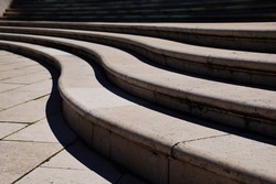 curving stone steps in exterior space. bright lights and shadows. background image. rectangular stone floor slab. S shape stair in abstract diminishing perspective.