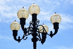 decorative street light closeup. antique style wrought iron light. blue sky. street lighting detail. white clouds. cast iron post. decorative park lamp. vacation and tourism. European travel concept.