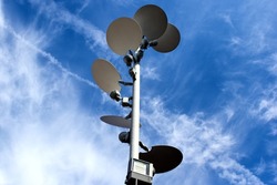 Large white dish shaped light deflectors and reflector lamp heads attached  to vertical pole. blue sky and white clouds. abstract low angle view. decorative street and city ambient lighting concept. 