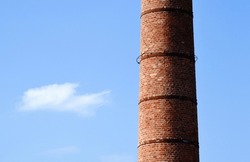 tall tapered large brick chimney stack closeup. rusty metal reinforcing straps. clear blue sky with white cloud. abstract composition. smoke, pollution and environment concept. large diameter cylinder