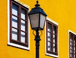 retro style street lantern. cast iron lamppost. colorful yellow stucco exterior wall background in old European town. old wood windows. urban street. travel and tourism concept. selective focus