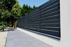 gray metal fence and gate. horizontal panels and gaps.  powder coated finish. diminishing perspective view. modern fence design concept. asphalt sidewalk. white stucco base and fence piers