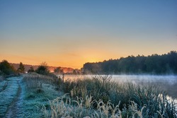 Autumn landscape - morning twilight over the lake. Fog over the water, the grass covered with frost