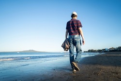 Man walking on the Milford beach with Rangitoto Island in the distance, Auckland.