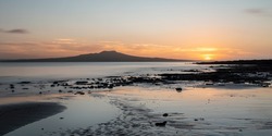 Sun rising over the clouds at Milford Beach in summer, Rangitoto Island in the distance.