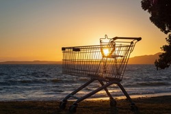 Backlit supermarket trolley abandoned on Milford beach, Rangitoto Island in the distance. Auckland.