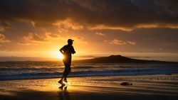 Silhouette man running on Milford beach at sunrise, Rangitoto Island in the background, Auckland. 