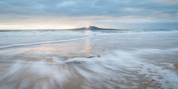 Sunrise at Rangitoto Island, slow movement of sea waves at foreground, Milford beach, Auckland. 