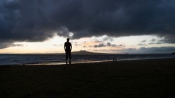 Silhouette of a man watching sunrise on Milford Beach with Rangitoto Island in the distance. Auckland. 