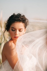 Close-up portrait of a brunette model girl in the role of a bride. Beautiful face, portrait at sunset in summer day.