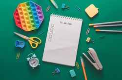 Colored various school supplies and an alarm clock on a green paper background. Back to school and education concept. Flat lay, top view, copy space. School plan and to do list.