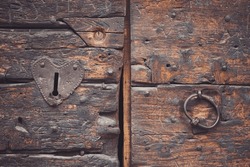 Ancient weathered door with heart shape lock keyhole and handle. Details of old vintage wooden door. Textured wooden church doors with heart-shaped decoration, a ring as a handle and a keyhole.