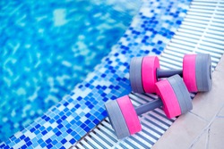 A swimming pool on summer day outdoors. Top view of plastic dumbbells for aqua fitness. Sportive equipment for aqua aerobics.
