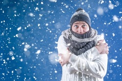 Warm. A man in a white sweater in a winter knitted hat and scarf stands under the falling snow. Snowfall. Winter. A person freezes in cold weather.