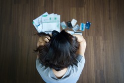 Top view of stressed young Asian woman hands holding the head trying to find money to pay credit card debt and all loan bills. Financial problem from coronavirus or covid-19 outbreak crisis concept.