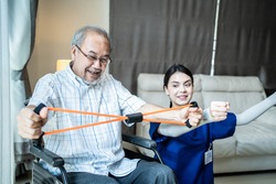 Asian Disabled senior elderly man on wheelchair doing physiotherapist with support from therapist nurse. Older handicapped man using resistance stretch band exercise for patient in home nursing care.