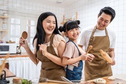 Asian happy family stay at home in kitchen spend time together baking bakery and foods. little kid with parents, father and mother dancing and laughing, enjoy parenting activity relationship in house.