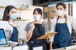 Asian Cafe manager leader explain job working to barista and waitress. Beautiful Coffeehouse worker wear mask due to Covid19 pandemic meeting and discuss work plan in store before restaurant reopen.