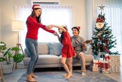 Asian happy family member enjoy sing Christmas song and dance together. Young little daughter feeling happy and excited to celebrate holiday Christmas Thankgiving party together with parents in house.