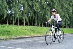 Asian young sport woman riding bicycle in the evening in public park. Beautiful athlete fit and firm girl in sportswear wear helmet, exercise by cycling workout for her health care wellness and fresh.