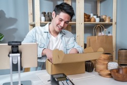 Asian young handsome man packing vase goods order in box for customer. Young attractive business man working to preparing parcel boxes checking ecommerce shipping online retail to sell at home store.